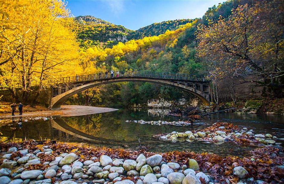 Greece in November.  Voidomatis river in Zagori with a bridge and yellow trees on the mountain