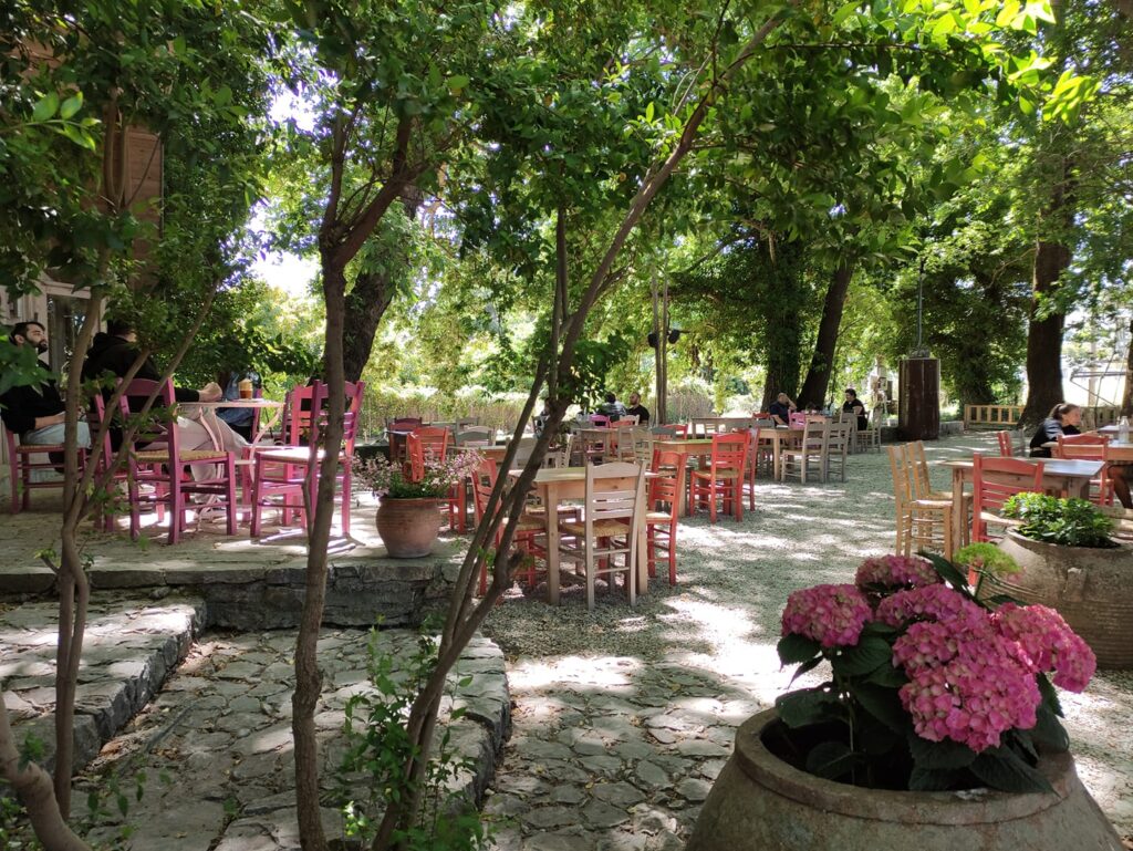 Tzitzikas Bio tavern garden with many trees and tables, chairs in Chania Crete Greece.