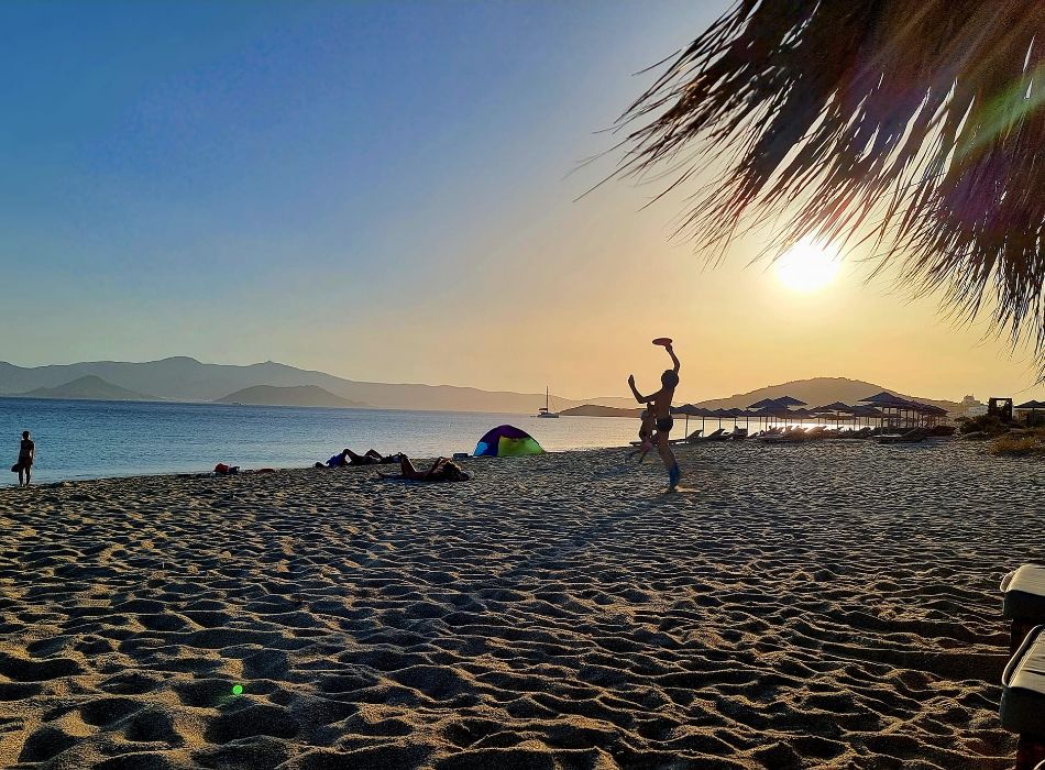 Sunset at a beach in Naxos, Greece, with people enjoying the serene atmosphere and golden sands.
