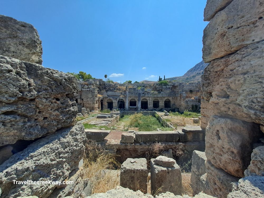  A view of Ancient Corinth's extensive archaeological site, including stone remnants of historic buildings and structures.