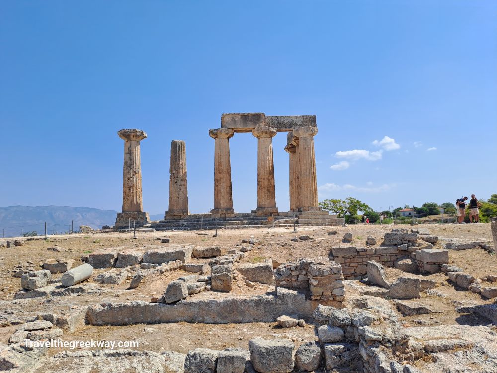 The remains of the Temple of Apollo in Ancient Corinth, showing tall columns under a bright blue sky.