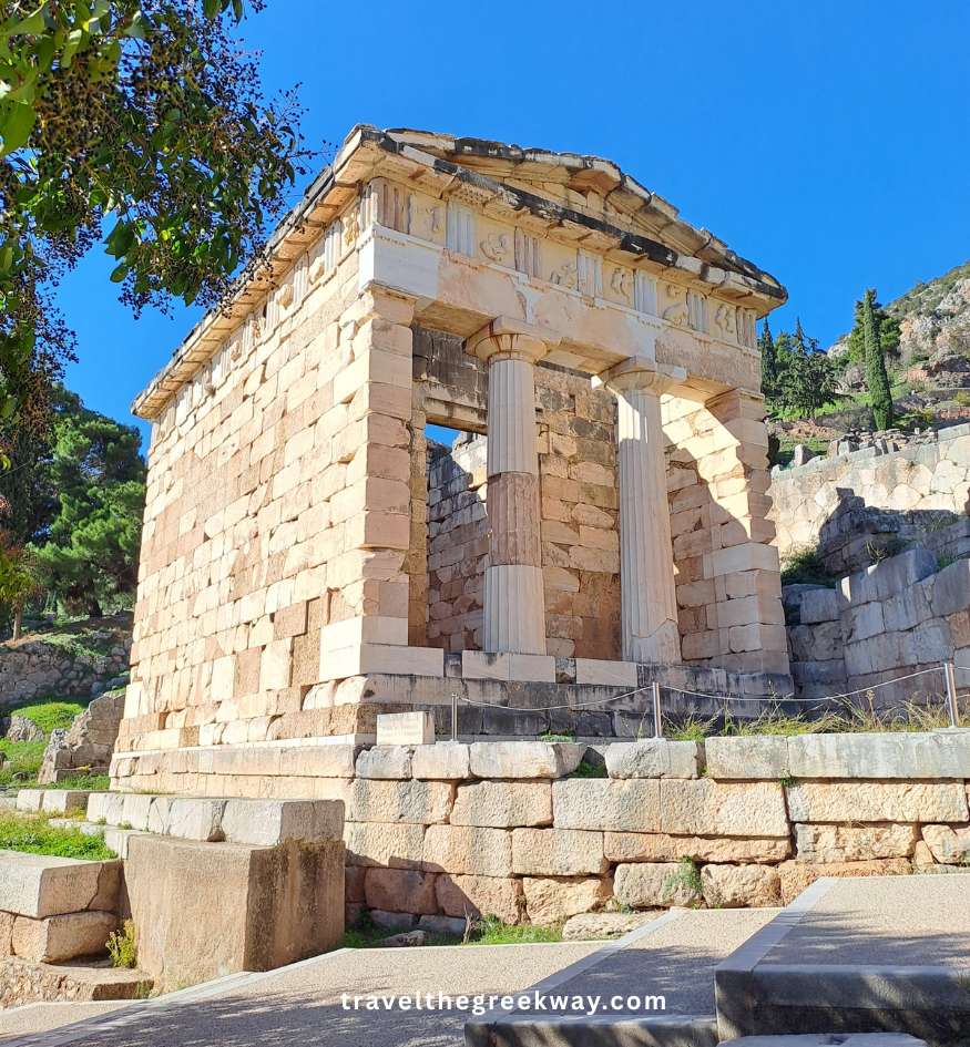 The Athenian Treasury in Delphi with its marble columns and bright blue sky above.