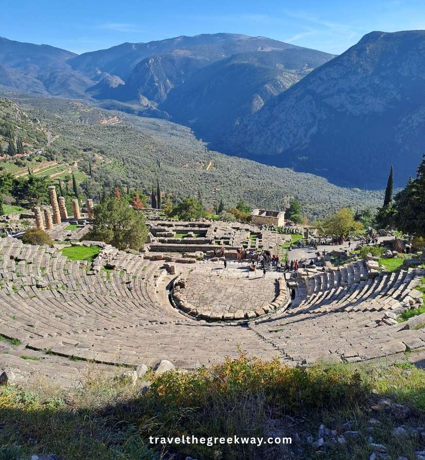 The ancient theatre of Delphi seen from above, surrounded by mountains and olive groves.