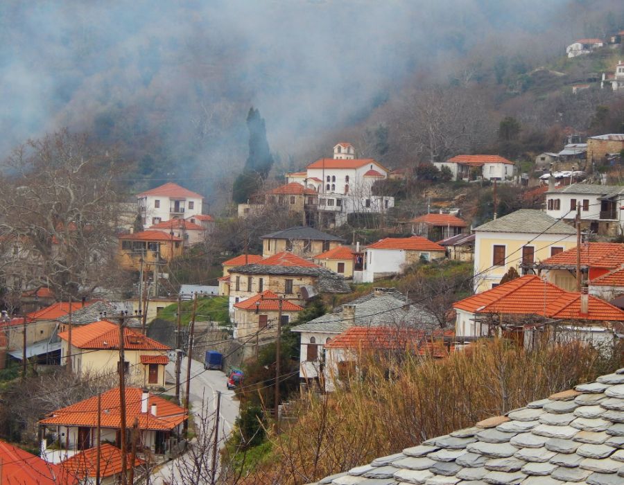 A foggy village in Pelion, Greece, with traditional stone houses and red-tiled roofs amidst a misty fall or winter atmosphere.