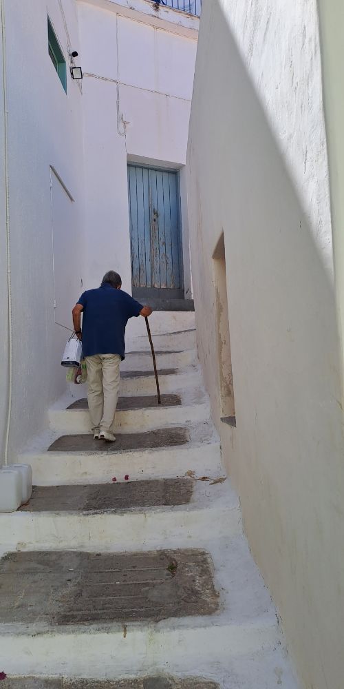 Older man climbing stairs with a cane in Kea island
