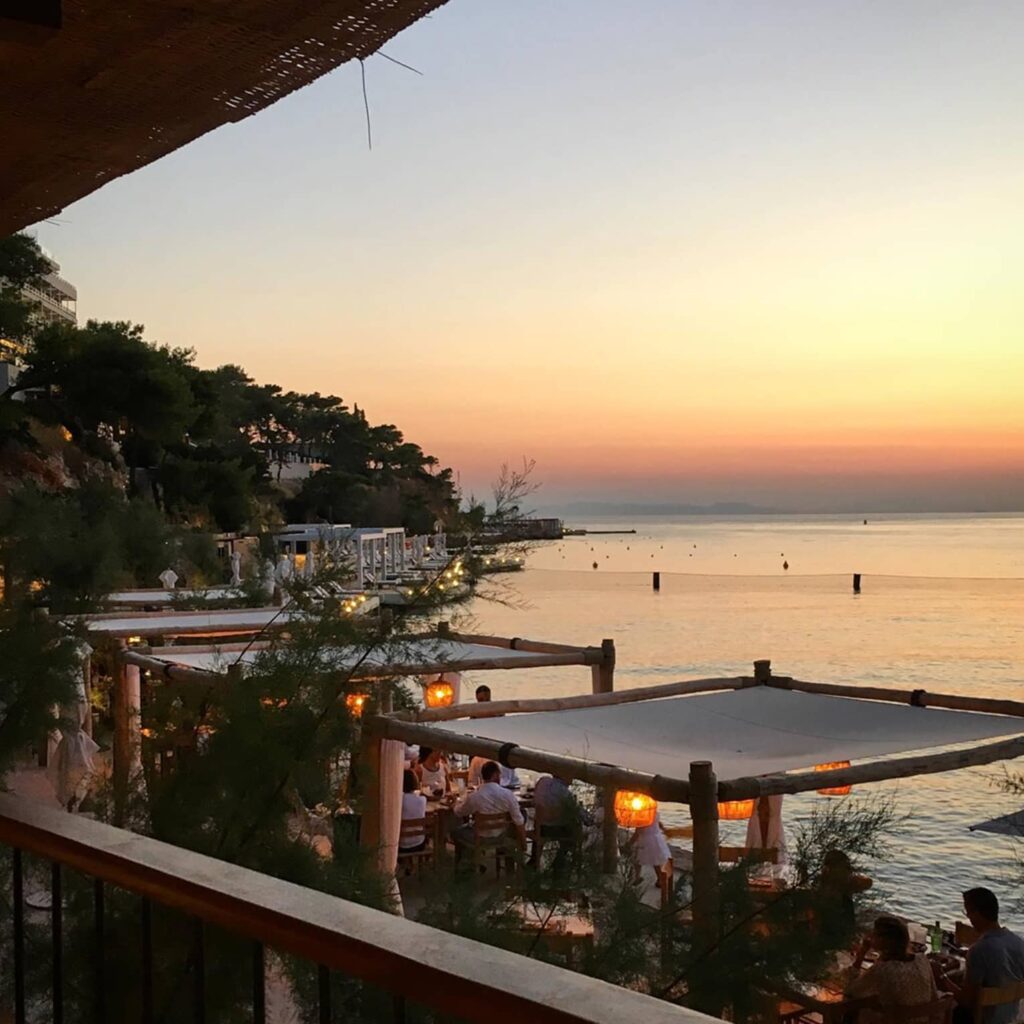  A serene sunset view at Tavern 37, part of the Four Seasons Hotel in Athens Riviera, with guests dining along the waterfront.