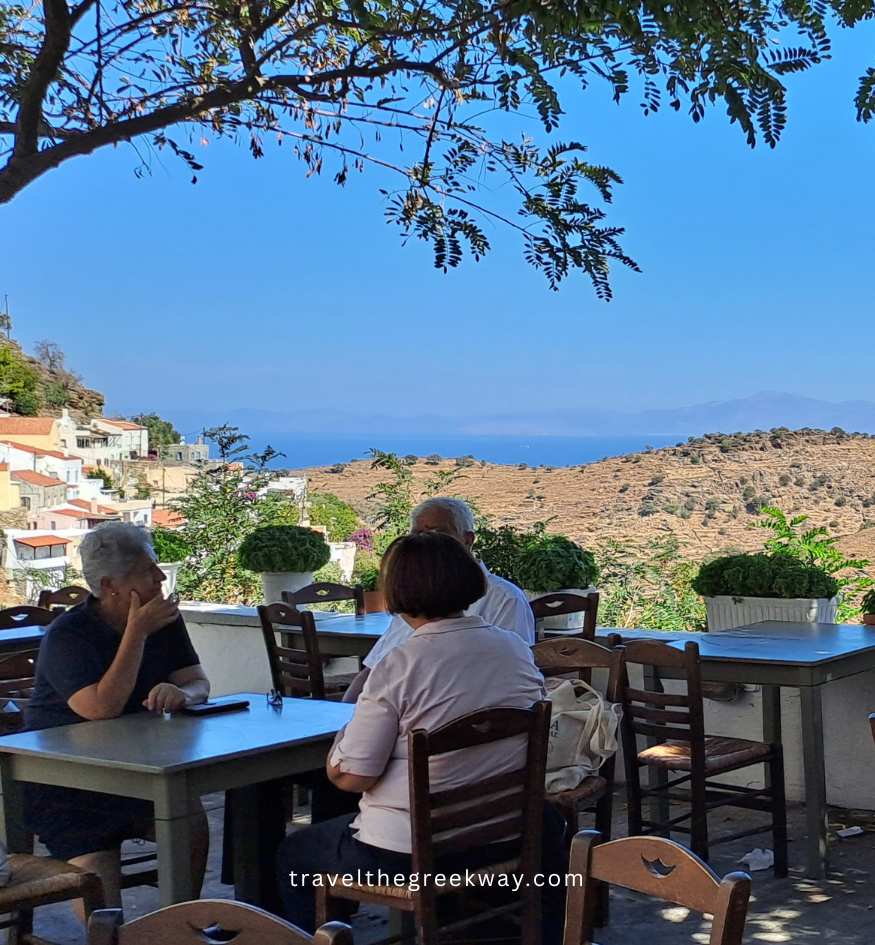 Travelers enjoying coffee at a traditional terrace cafe in Ioulida, offering panoramic views of Kea’s island rugged hills and the Aegean Sea in Greece.