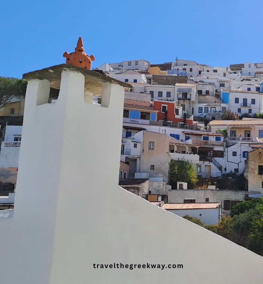 Close-up of a white chimney with a traditional ceramic topper against a backdrop of colorful, terraced houses in Ioulida, Kea island, Greece.