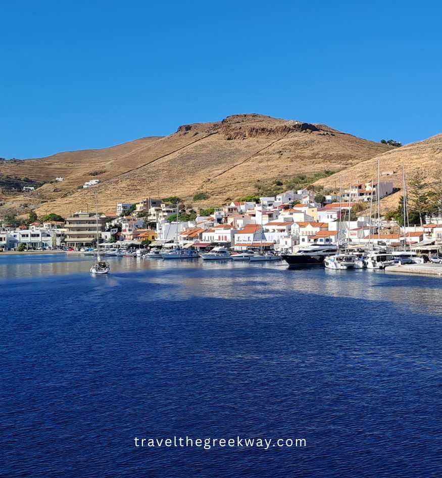 Harbor view of Korissia with boats, waterfront houses, and dry hills in the background on Kea island, Greece.