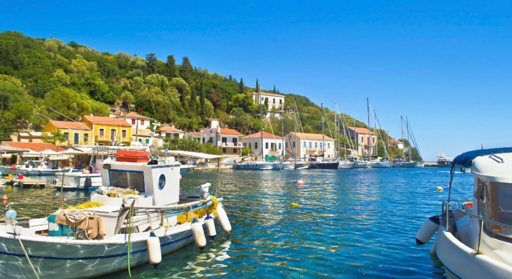 A serene coastal view of Ithaca Greece seafront village Kioni with colorful fishing boats lining the picturesque shores against a backdrop of clear blue skies and gentle waves.