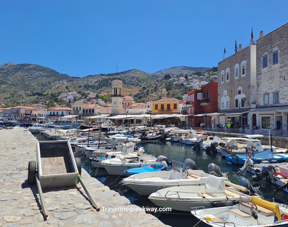 Best Things to Do in Hydra Greece. View of Hydra Island’s scenic harbor with boats, stone buildings, and hillside houses in the background.