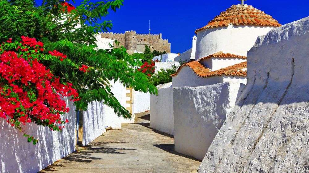 Best Places to Visit in Greece: Patmos island alley with a church and red flowers