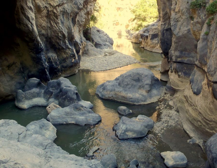 Rocky stream flowing through Kourtaliotiko Gorge in Crete, with large boulders and narrow passageways formed by the surrounding cliffs.