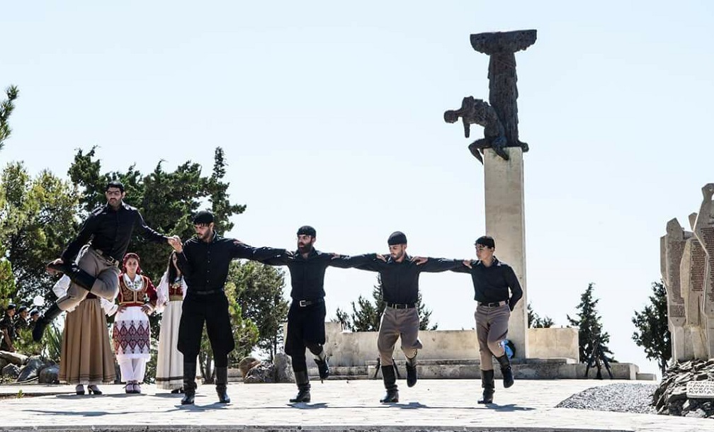 Traditional Cretan dancers in black costumes performing a folk dance in front of a monument at the Arkadi Monastery in Rethymno, Crete.