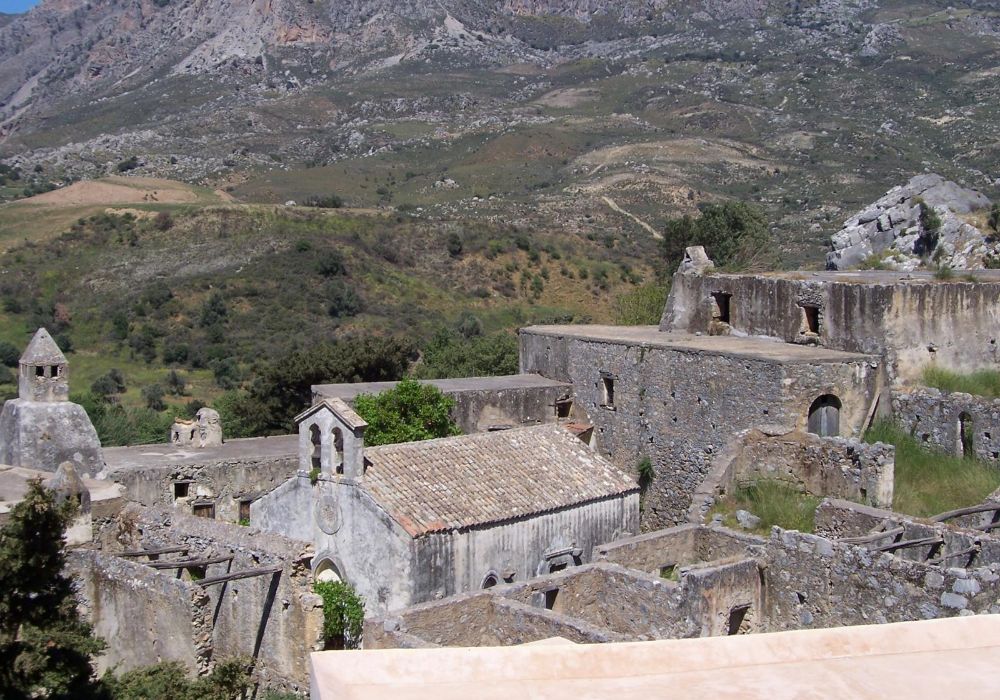 Ruins of an old monastery in Kato Preveli, Rethymno, Crete, set against a backdrop of rolling hills and rugged mountains.