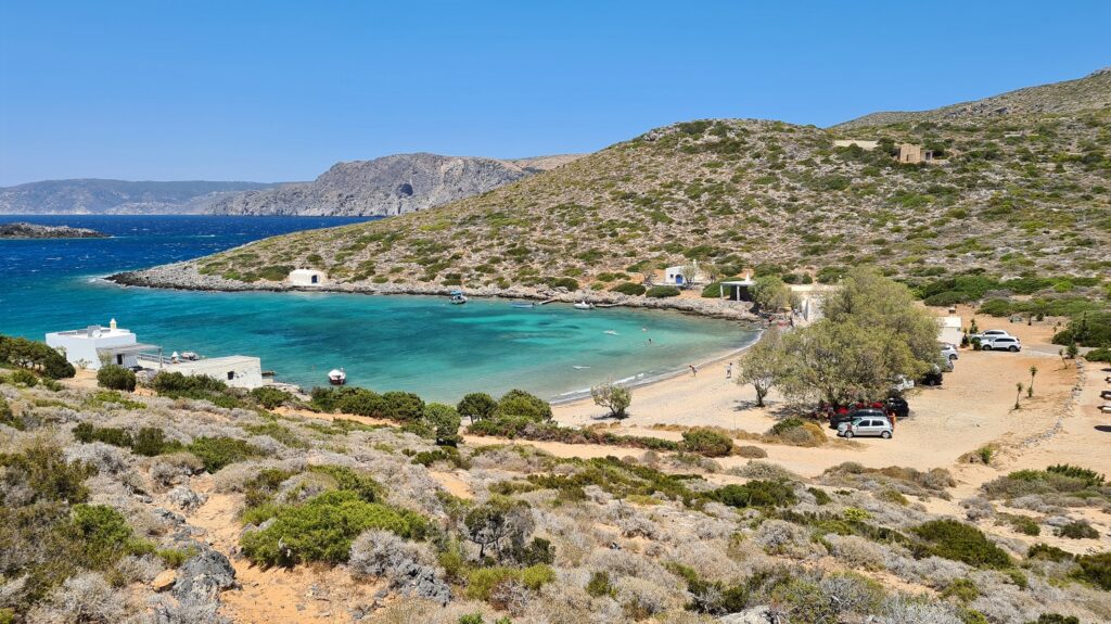 A Sandy Beach with trees, some White Washed houses with blue sky in Limnionas Beach Kythira Greece.