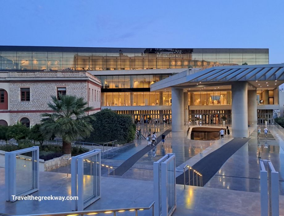 The illuminated entrance of the Acropolis Museum in Athens during the evening, showcasing its modern architecture and reflective surfaces.