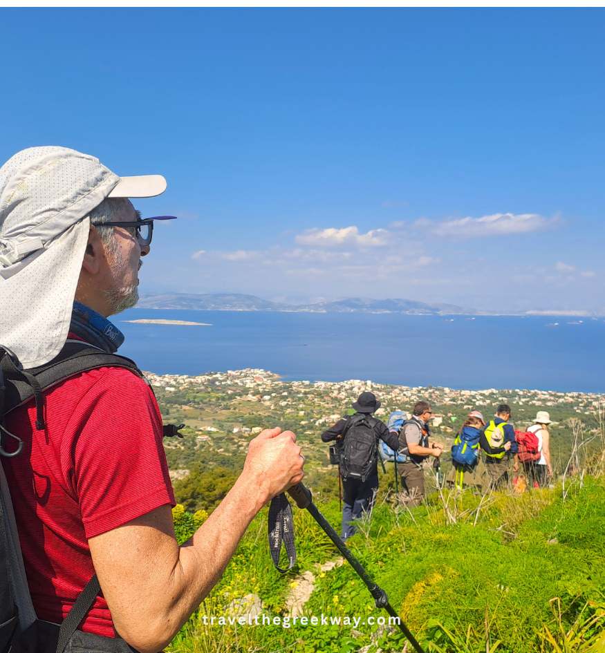 A hiker with trekking poles looking out over the sea and coast from a high scenic trail on Aegina Island, Saronic Gulf, Greece.