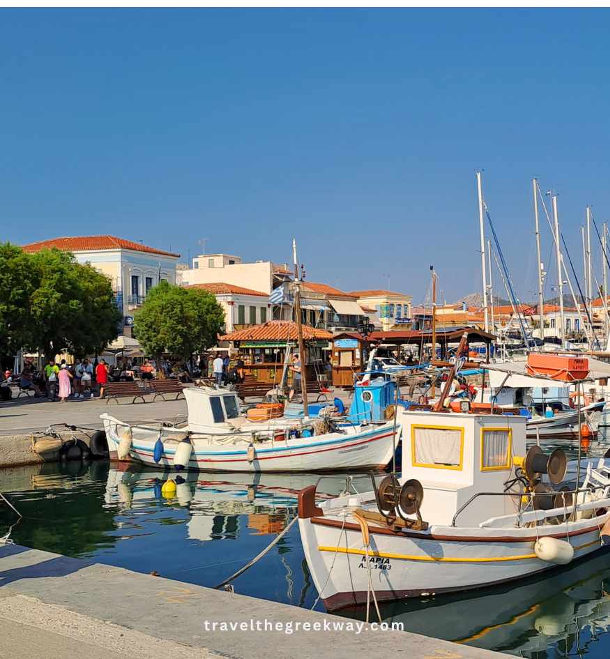 Traditional white fishing boats moored at the lively main harbor of Aegina Town on Aegina Island, Saronic Gulf, Greece.