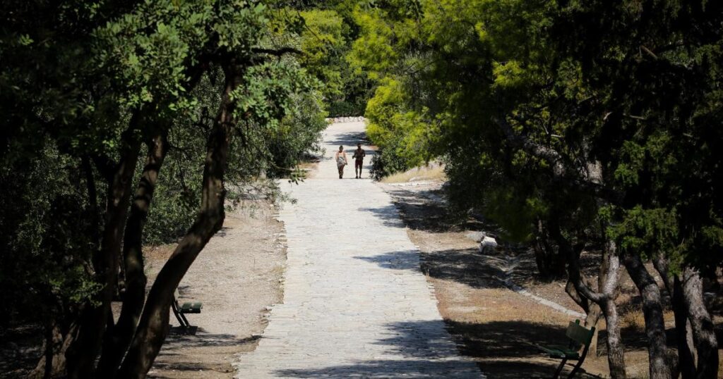 A couple walks along the paved trails with trees in Philopappou Hill in Acropolis of Athens