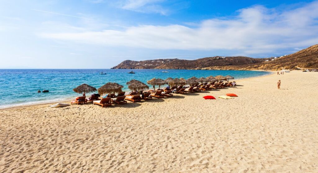 A sandry beach with some umbrellas and people in Elia Beach in Mykonos Island.