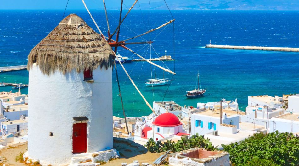 A whitewashed windmill on the top of the hill. A Greek Church and some houses with view at the sea. In Mykonos Island. 