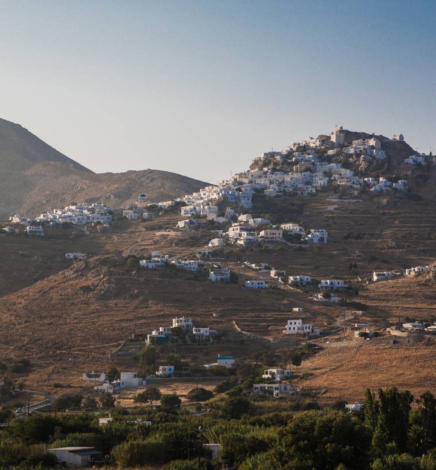 View of the whitewashed Chora village perched on a steep, rocky mountain slope during the golden hour in Serifos, Greece.