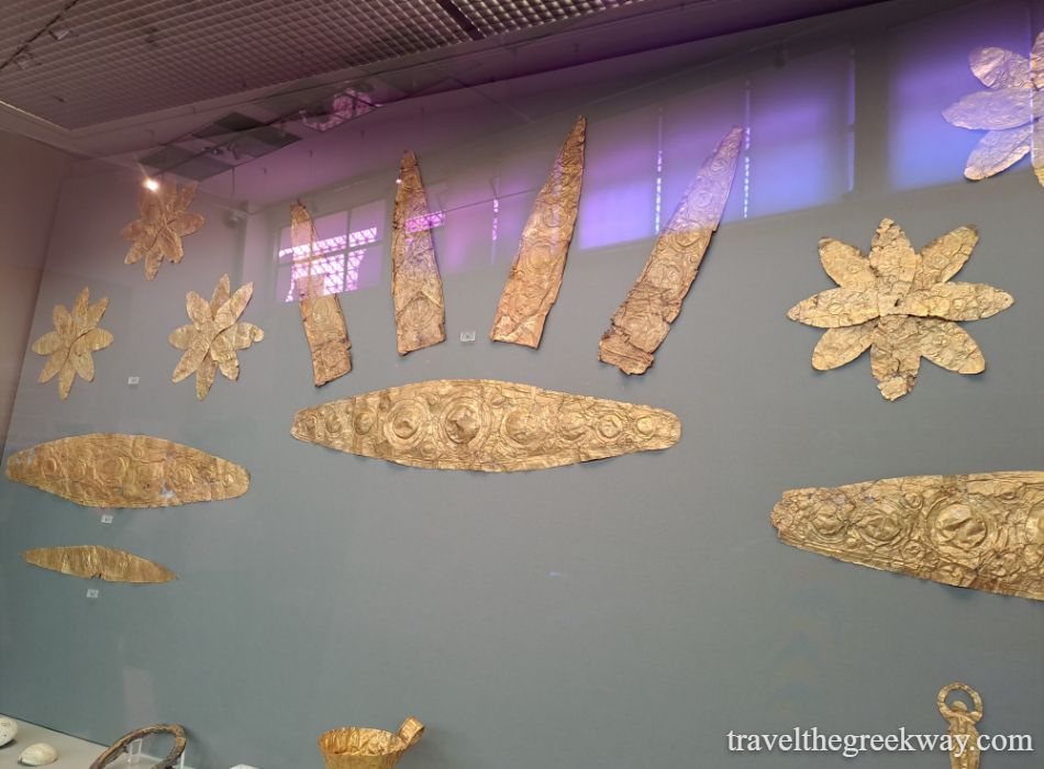 Golden ornaments from Mycenae, Greece, showing detailed designs in a museum display of ancient burial treasures.