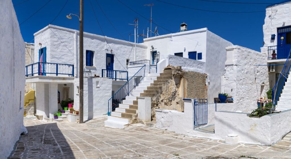 A white washed alley with houses with blues doors and windows in Kimolos island in Greece.