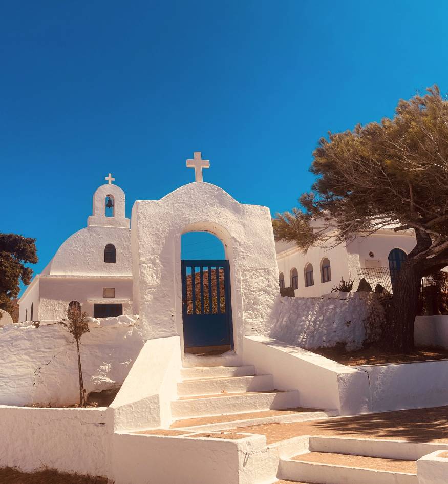 A traditional white Cycladic church with a blue door and stone steps under a bright blue sky in Serifos, Greece.