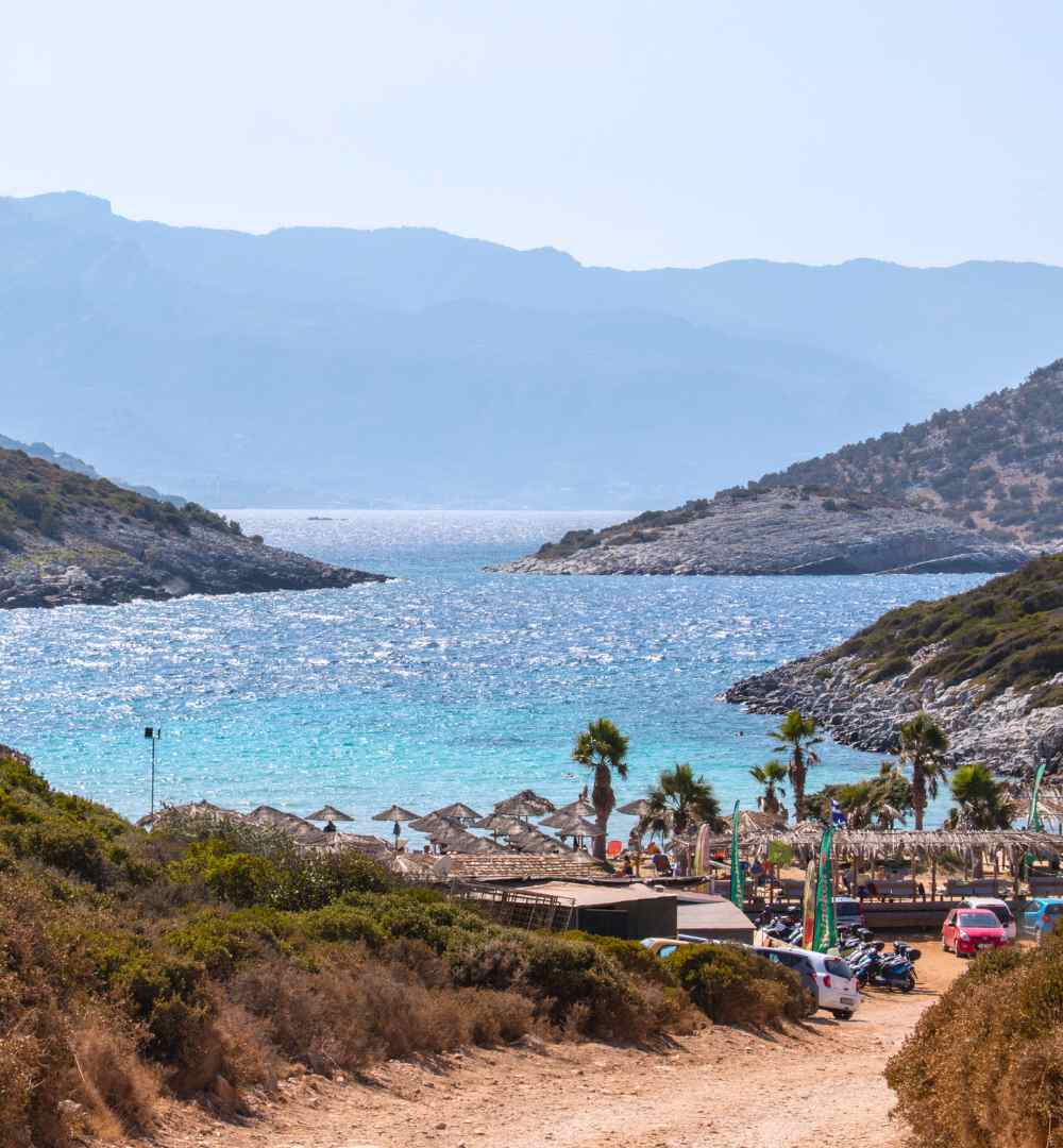 Aerial view of a secluded cove at Livadaki Beach, Samos, Greece, featuring turquoise water and straw umbrellas.