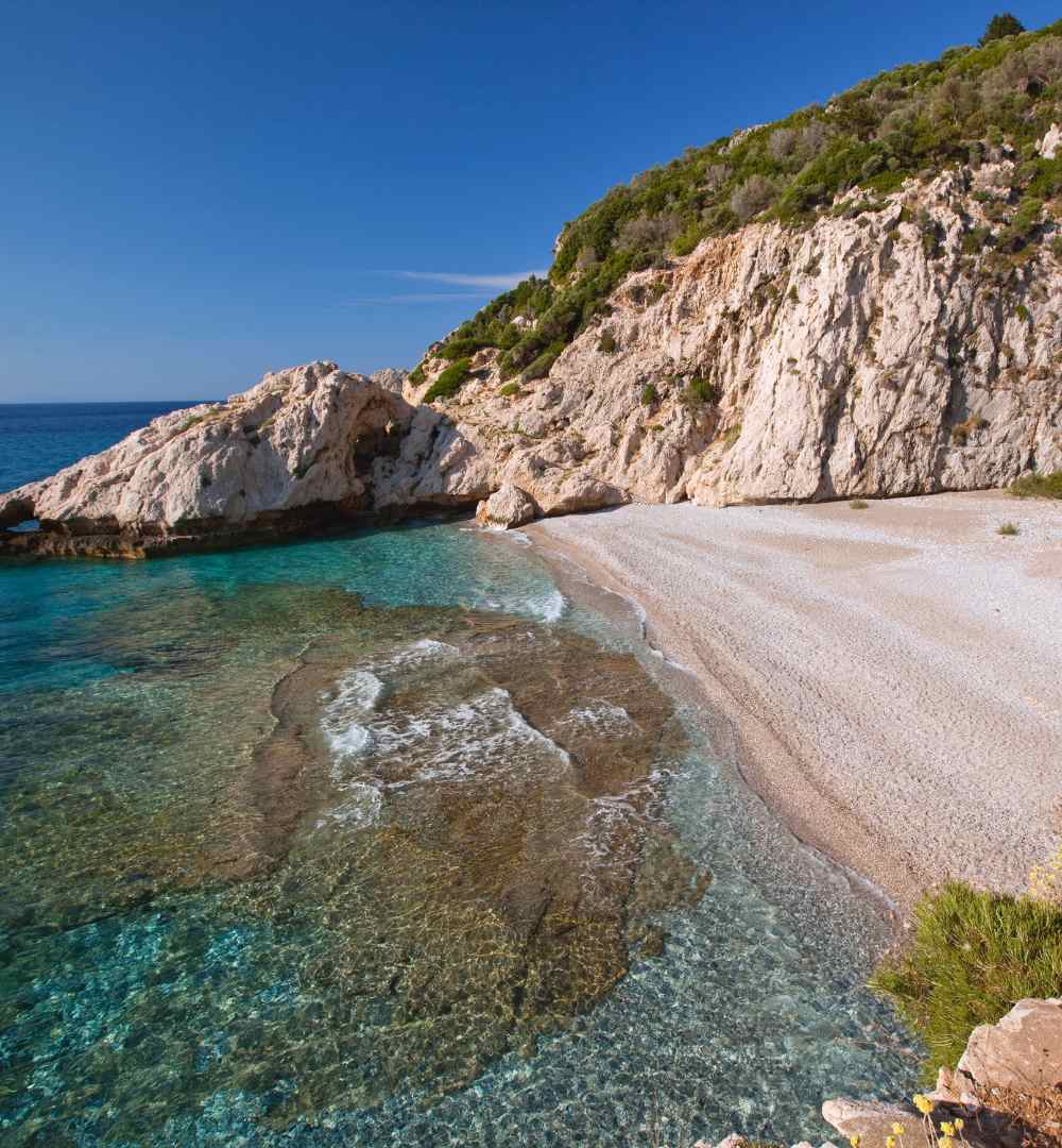 Pristine white pebble beach at Seitani, Samos, Greece, tucked between rocky cliffs and transparent water.