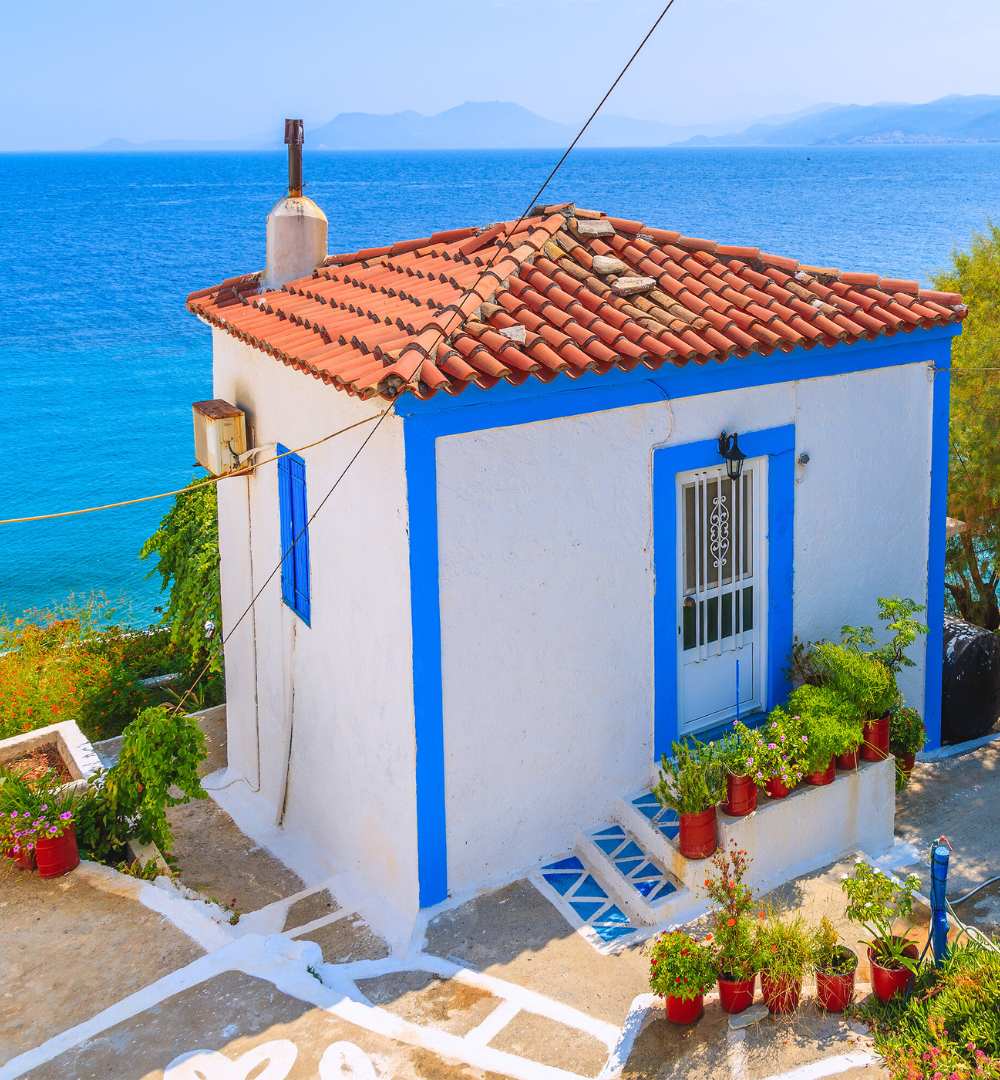 Charming small white house with blue trim on a cliffside overlooking the Aegean Sea in Samos, Greece.