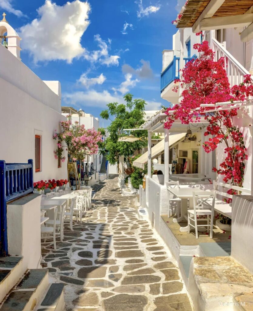 A whitewashed alley with plants and some tables and chairs in a sunny day. Paros Greece.