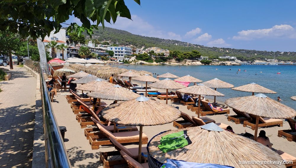 Agia Marina beach in Aegina with many sunbeds and straw umbrellas.