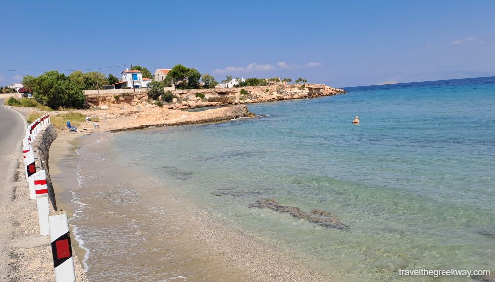 A sandy beach by the coastal road with one single swimmer. 