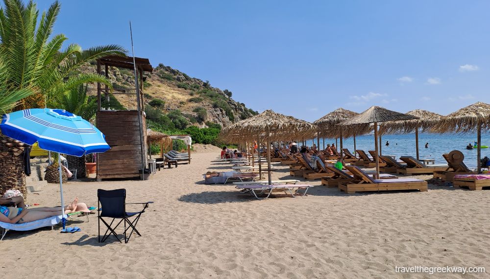 Marathonas B sandy beach in Aegina with many sunbeds and straw umbrellas.