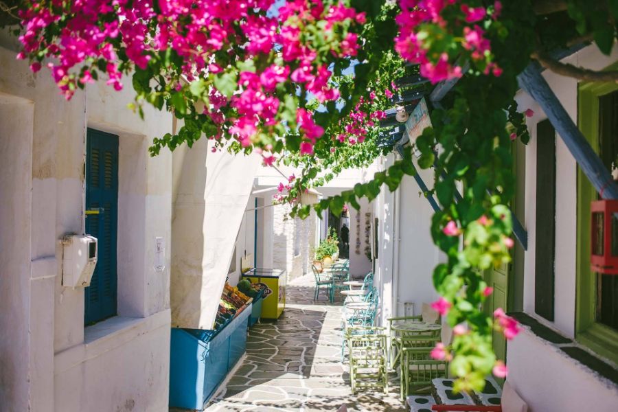 A beautiful alley with whitewashed houses with colorful windows, tables and chairs and a voukamvilia in Kythnos Greece.