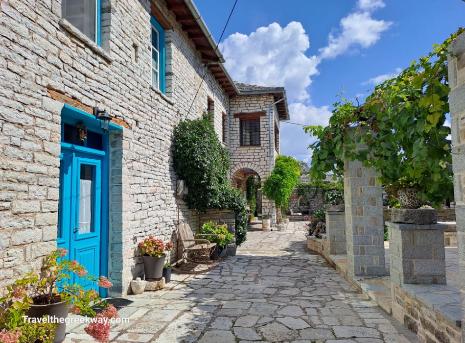 A beautiful yard with stone houses with blue doors and flowers in Monodendri Greece.