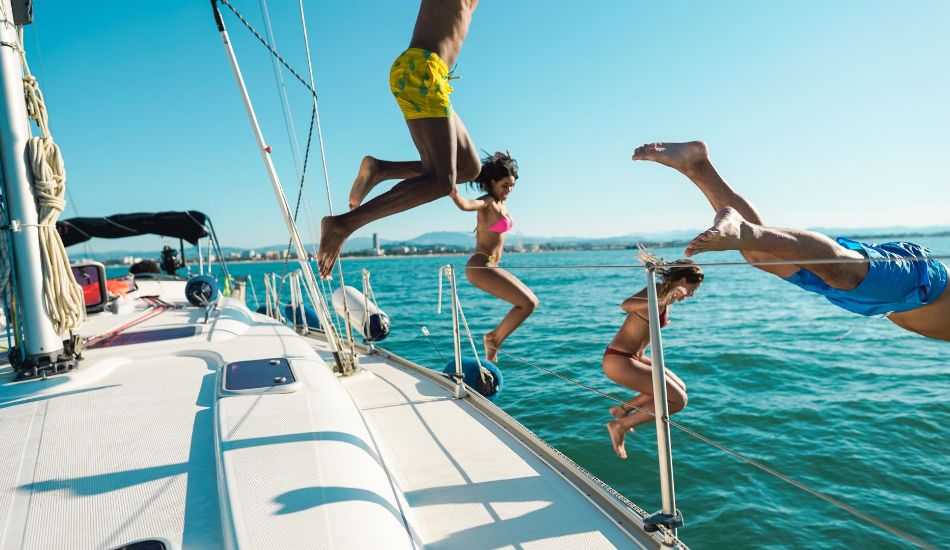 A group of young people jumping off a yacht into the sea in summer. 