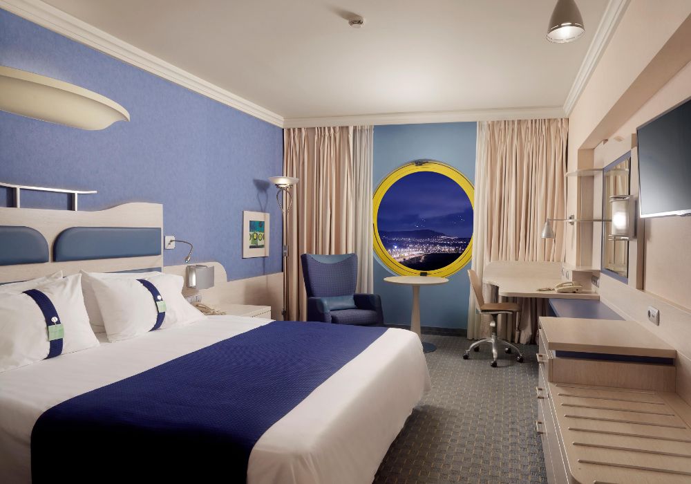 Holiday IIn Athens bedroom, one of the Best Athens Hotels Near the Airport. Decorated in blue and white colors with a round window. 
