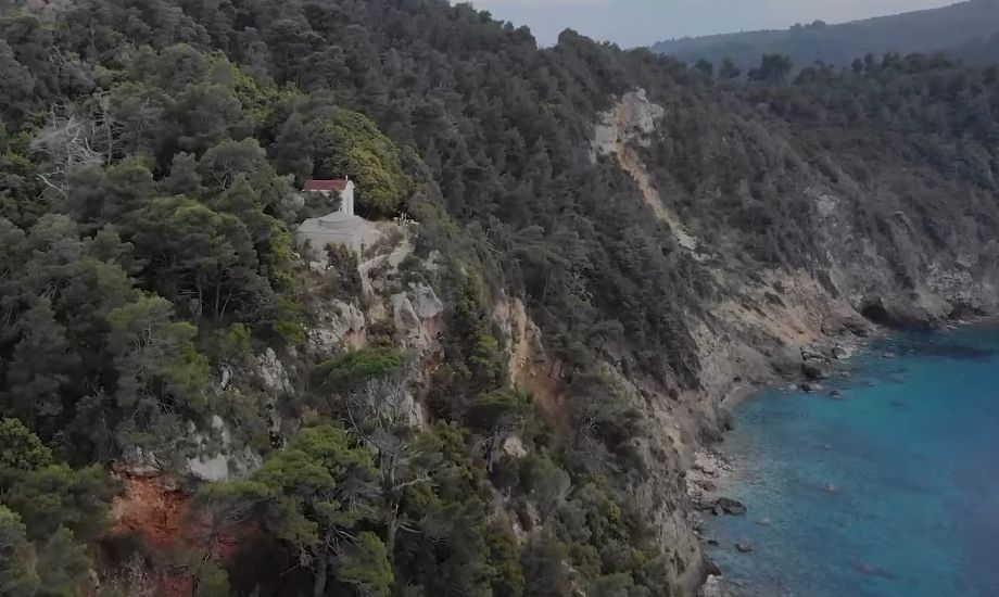 A remote and rugged area with very high mountains in Alonissos, with a small church surrounded by pristine turquoise waters. 