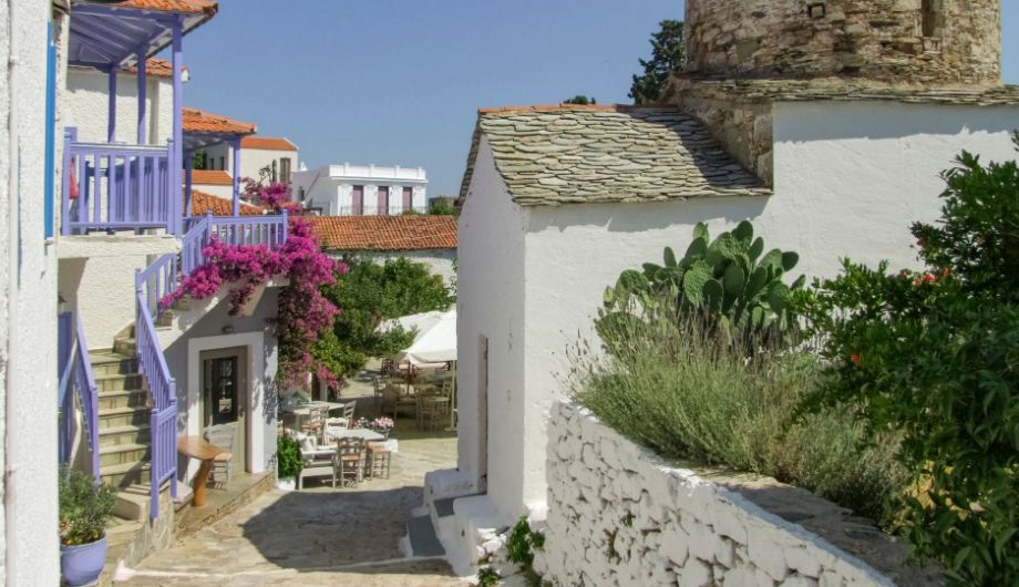 An enchanting view of the old traditional village perched atop a hill on Alonissos Island, Greece. Narrow cobblestone streets wind through whitewashed houses adorned with vibrant bougainvillea.