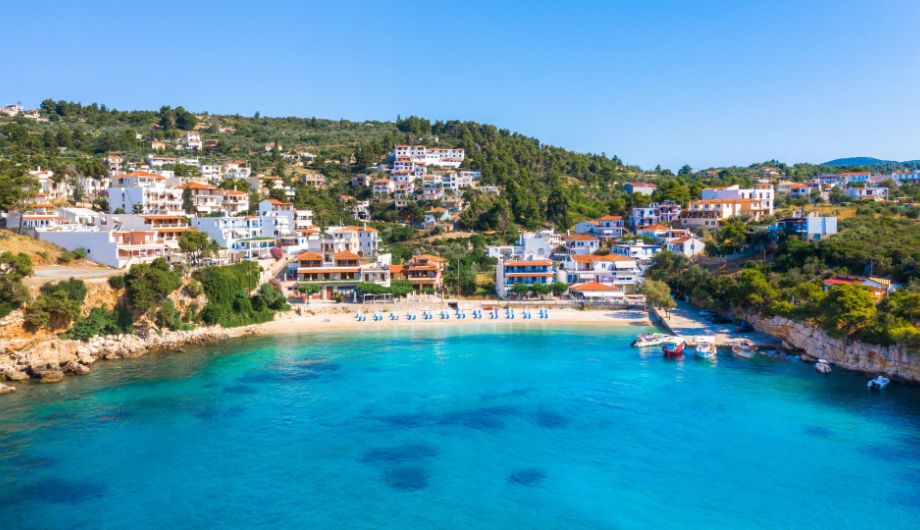  quaint coastal village nestled along the shoreline of Alonissos Island, surrounded by verdant hills and overlooking the shimmering blue waters of the Aegean Sea. 