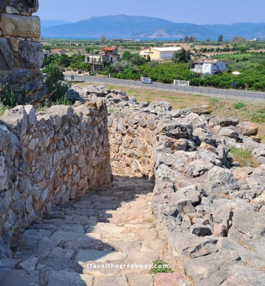 A stone path leading down from the ancient fortifications of Tiryns, overlooking the lush green valley and mountains in the distance, near Nafplio, Greece.
