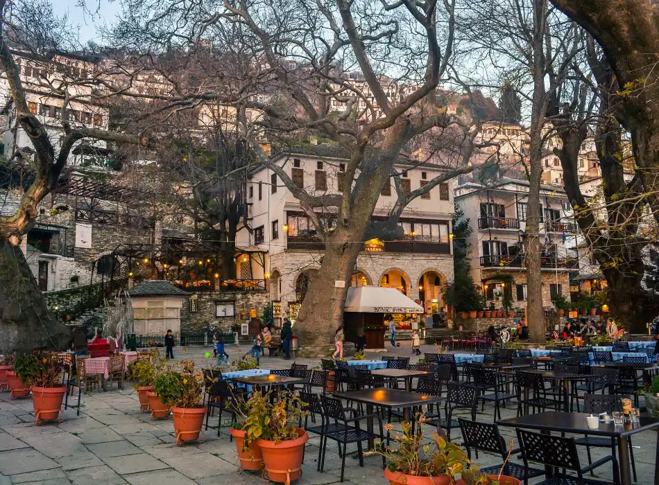 The central square of Makrinitsa with tables and chairs, large trees and houses. 