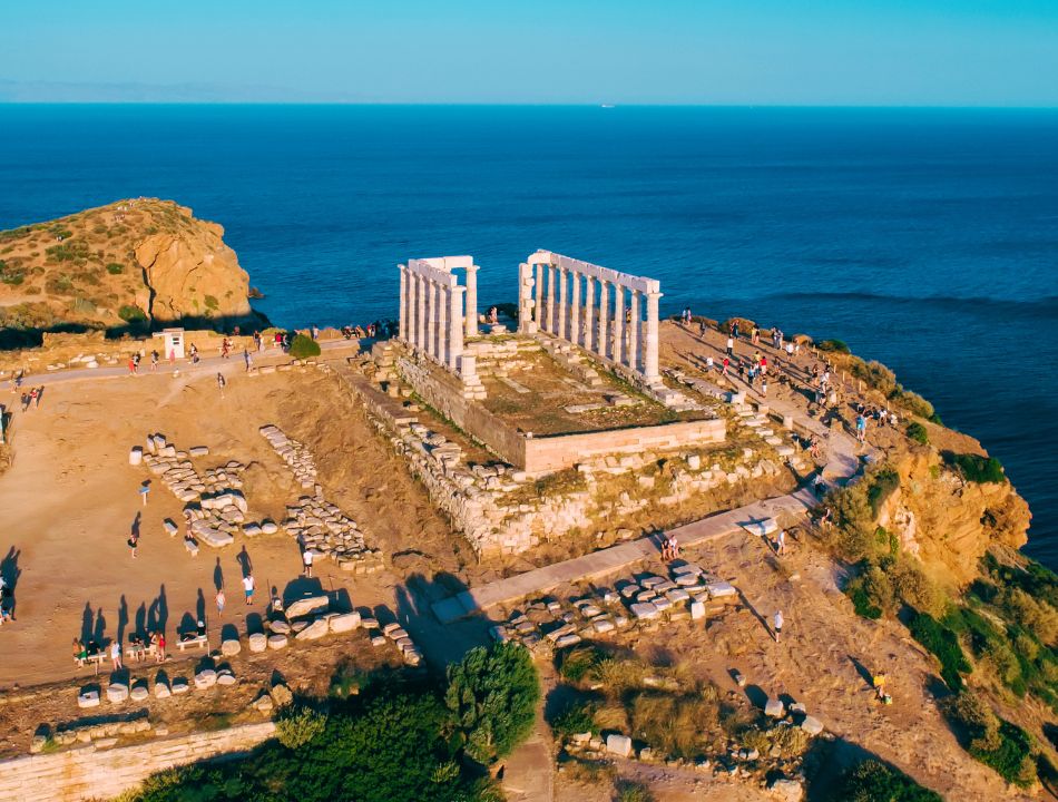 The Temple of Poseidon in Cape Sounion, Athens in Greece at sunset with people visiting. The photo is taken from a drone. 