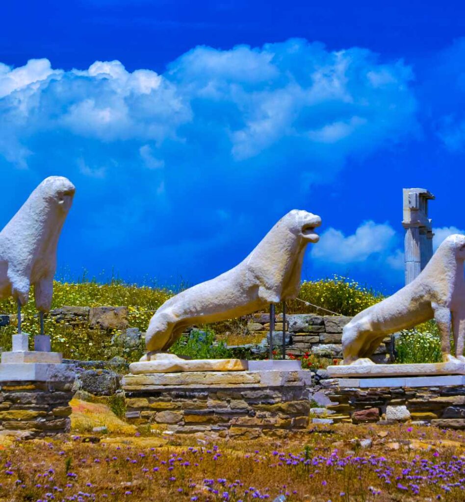 Marble lion statues at the archaeological site of Delos under a bright blue sky.