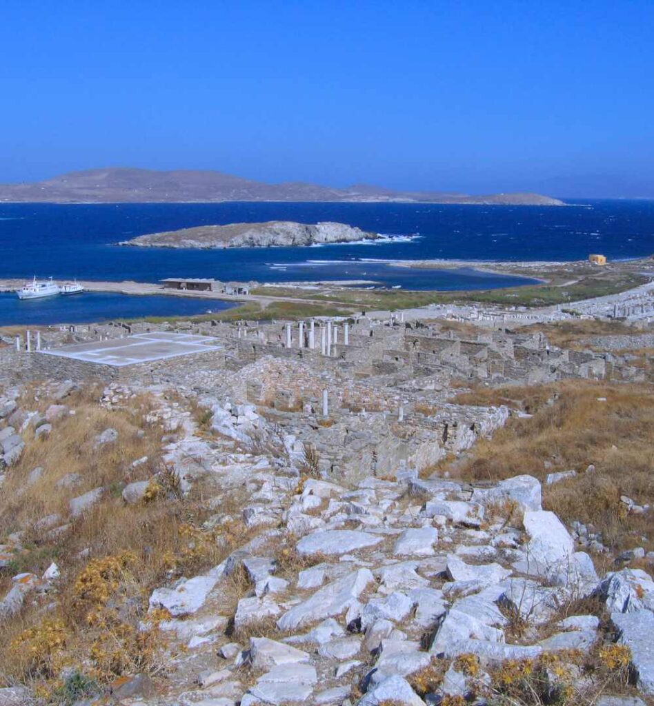 Ruins of ancient Delos with stone foundations overlooking the Aegean Sea near Mykonos.