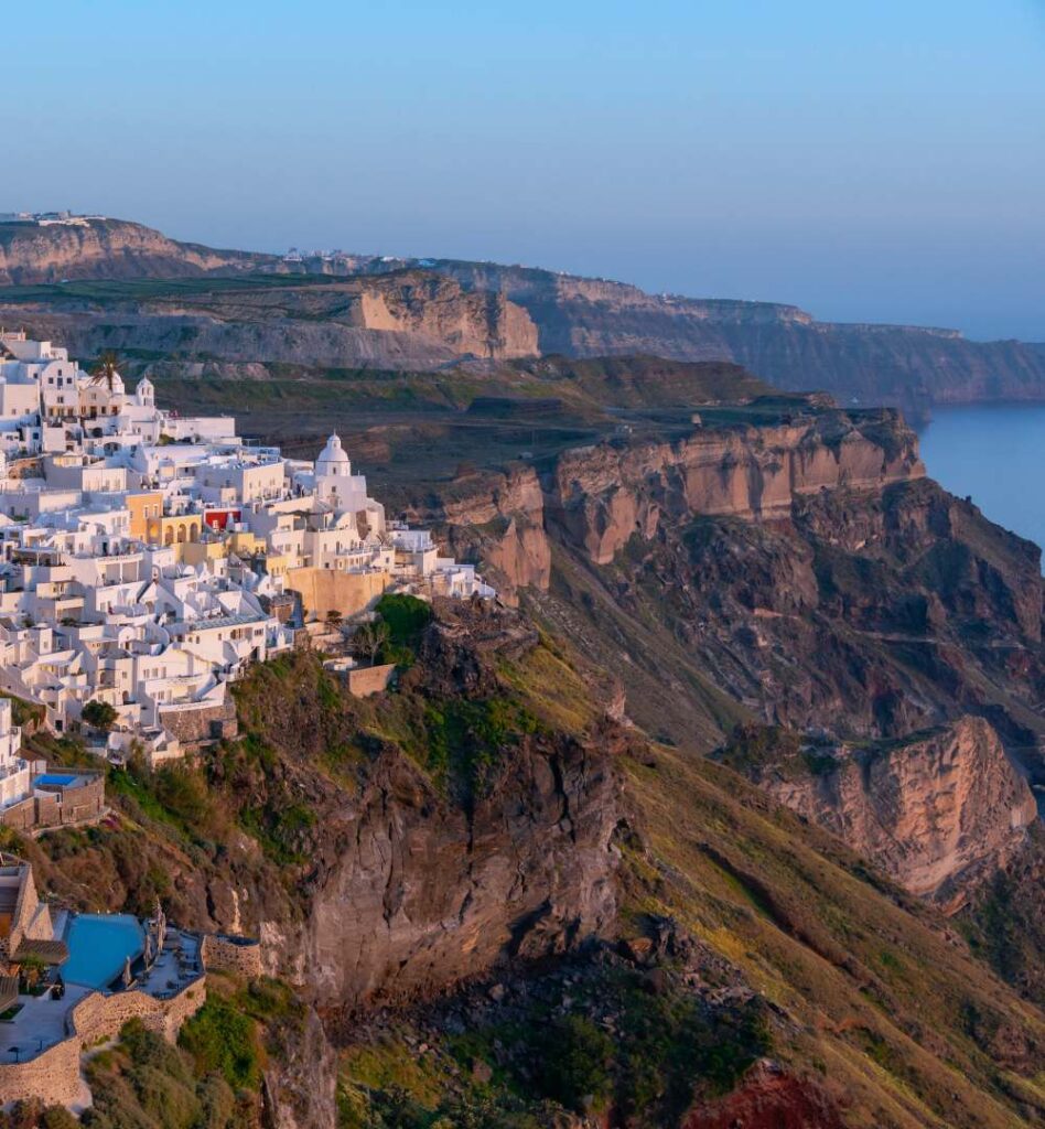 Santorini caldera view with steep volcanic cliffs and boats in the deep blue sea.
